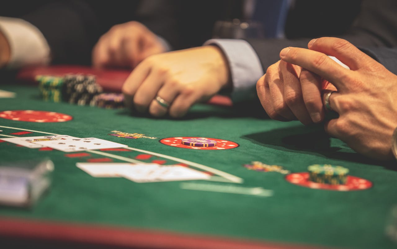 iWin88 official malaysia Hands playing blackjack in a casino setting with cards and chips on a green table.